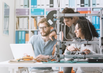Group of engineering students using a 3D printer and a laptop in the lab, technology and learning concept