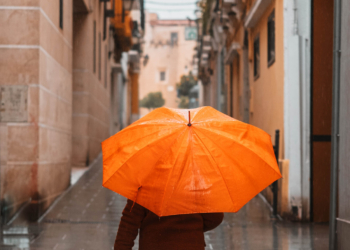 Girl with an orange umbrella protecting herself from the rain walking down a lonely narrow street